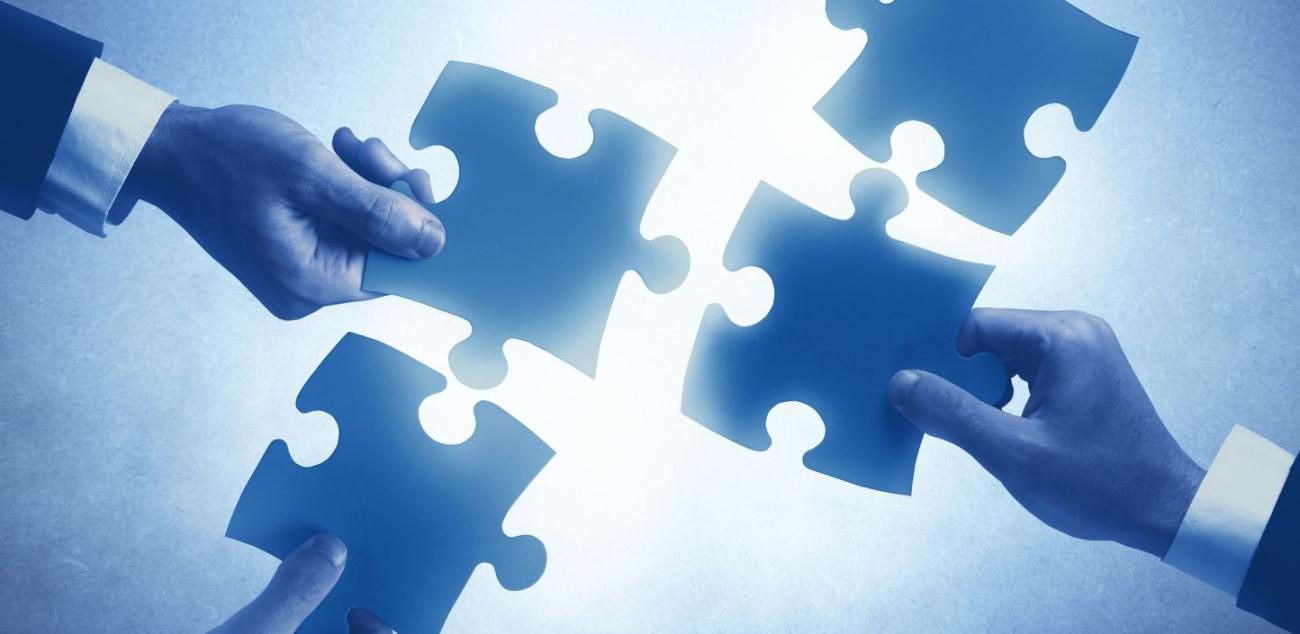 Hands joining jigsaw puzzle pieces, illustrating coordination between users, experts and suppliers.